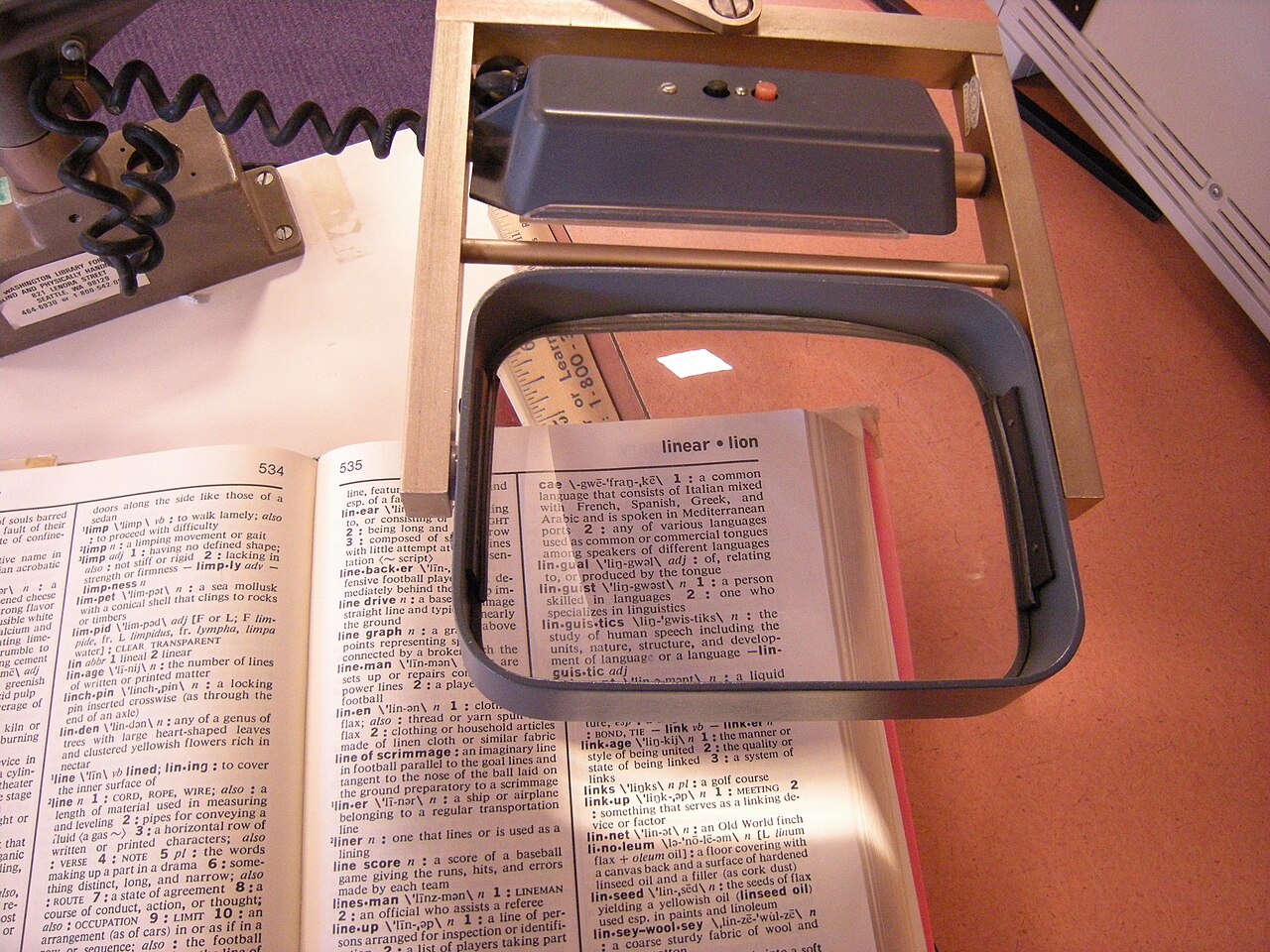 A desktop magnifier held over printed pages in an open book