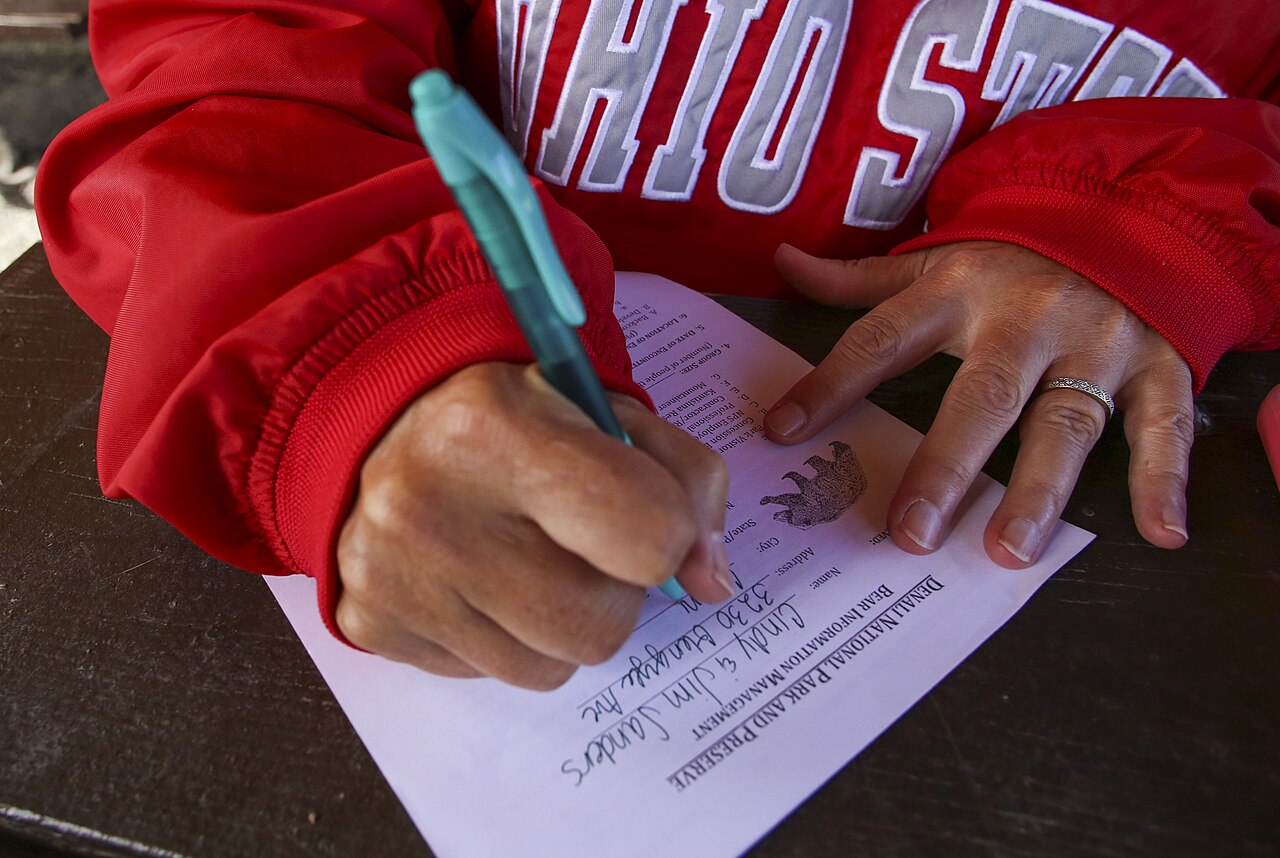 Close-up of hands filling out a paper form with a pen