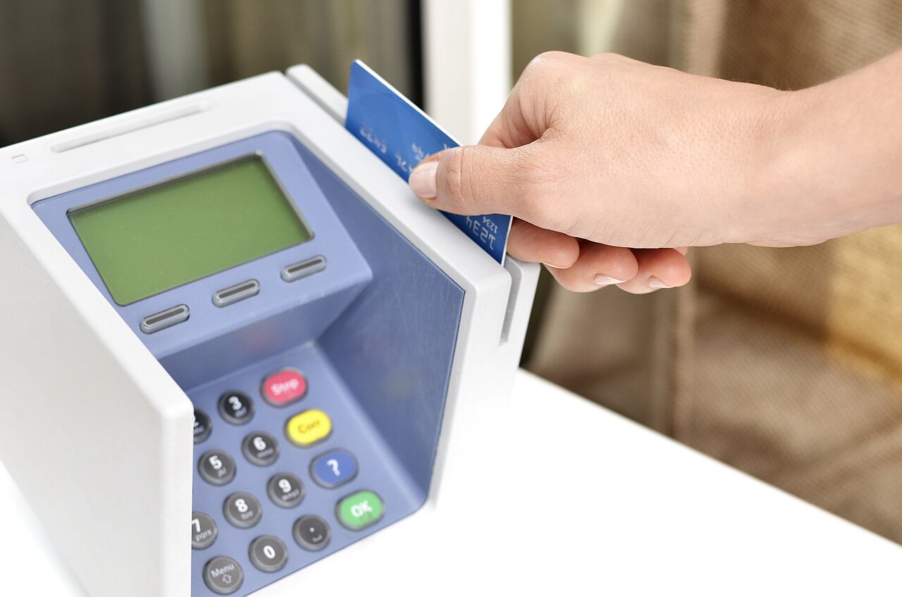 A hand swiping a blue card through a payment terminal